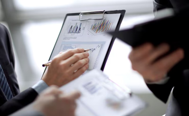 세 개의 모니터에 복잡한 주식 차트와 금융 데이터가 띄워져 있는 전문가의 책상 모습