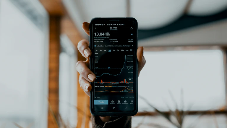 주식 앱이 켜진 스마트폰을 들고 있는 손